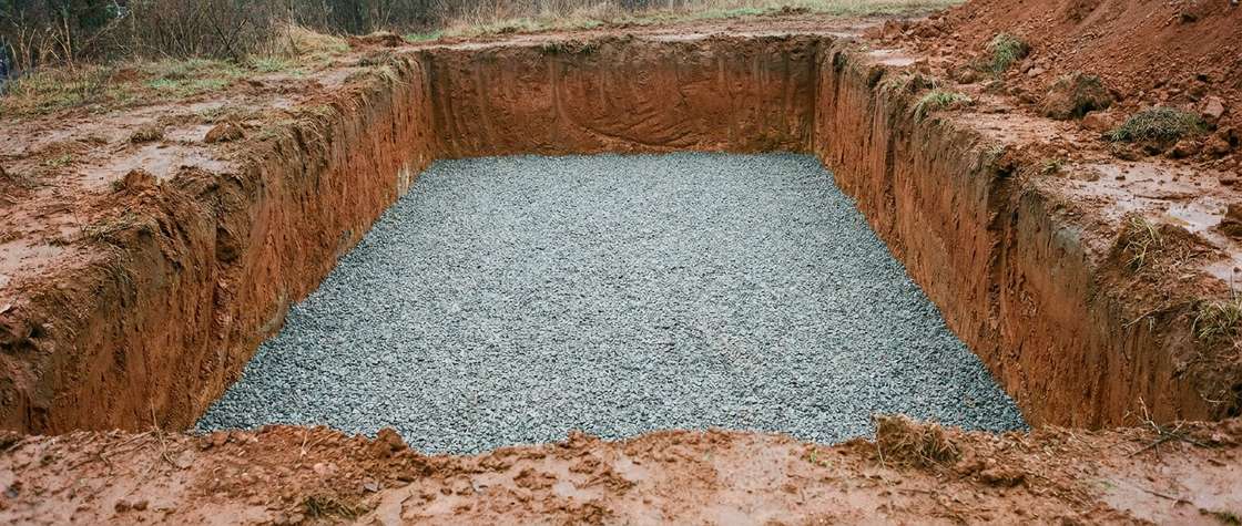 A level compacted bed of crushed gravel at the bottom of a rectangular excavation in red clay