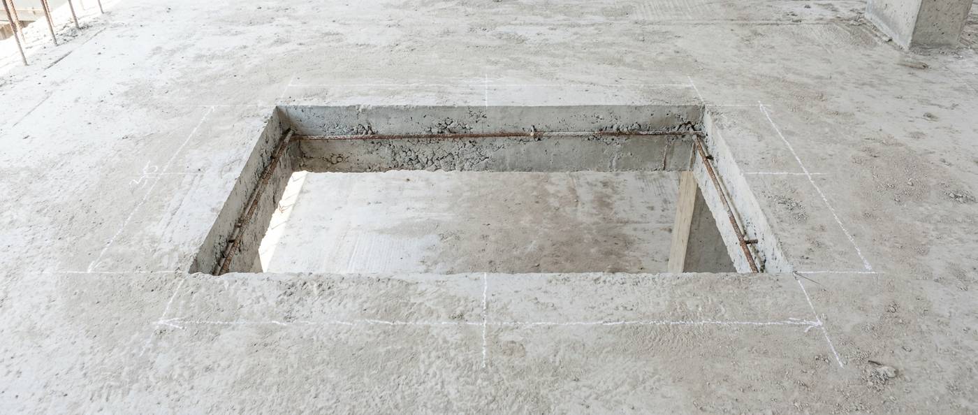 A neat rectangular saw-cut opening in a concrete garage slab showing slab thickness and reinforcing bar
